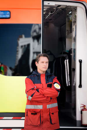 Paramedic with crossed arms standing near ambulance auto outdoors
