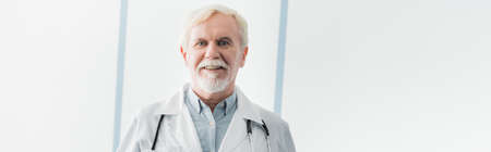Website header of elderly doctor in white coat looking at camera in clinic