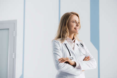 Blonde doctor with crossed arms looking away in clinicの写真素材