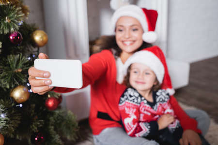 Selective focus of mother and daughter in santa hats taking selfie at home