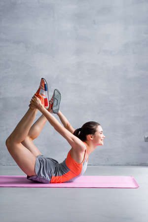 Side view of sportswoman training on fitness mat on gray background