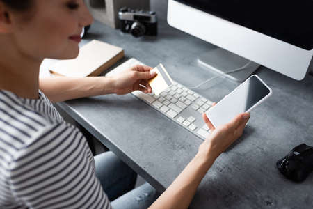 Selective focus of young freelancer using smartphone and credit card while working at home