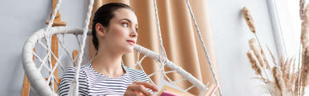 Website header of young woman with book looking away in hanging armchair