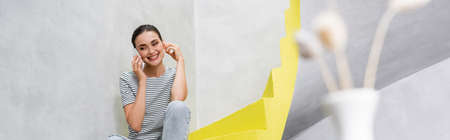 Panoramic shot of young woman talking on smartphone on stairs at home