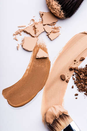top view of cosmetic brushes with face foundation brushstrokes and powder on white