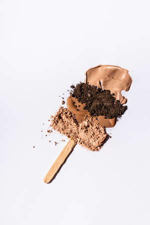 top view of beige face foundation brushstrokes and eyeshadow powder with wooden stick on white backgroundの写真素材