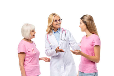 Doctor pointing with hand near women with pink ribbons of breast cancer awareness isolated on whiteの写真素材