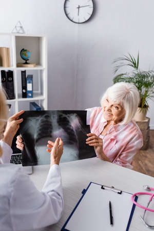 Doctor and elderly woman holding and looking at chest x-ray at workplaceの写真素材