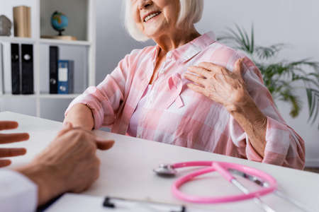 Cropped view of elderly woman with hand near pink ribbon near doctorの写真素材