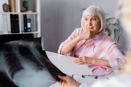 Selective focus of pensive senior woman sitting near doctor with chest x-ray