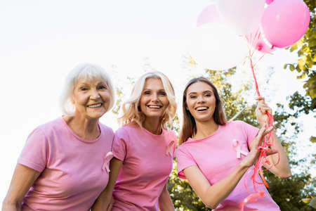 Three women with ribbons of breast cancer awareness near balloons outdoors