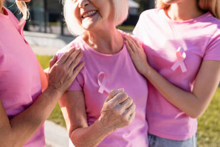 Cropped view of woman with pink ribbon showing fist standing near women outdoorsの写真素材
