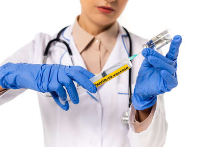 Cropped view of doctor picking up vaccine in syringe with covid-19 lettering isolated on whiteの写真素材
