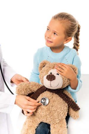 Smiling child holding soft toy near doctor with stethoscope isolated on whiteの写真素材