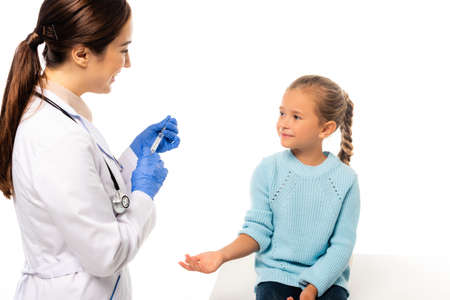Smiling pediatrician in latex gloves holding syringe near child isolated on whiteの写真素材