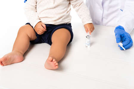 Cropped view of doctor holding syringe near toddler boy and jar with vaccine isolated on white