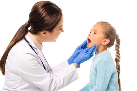Selective focus of smiling pediatrician in latex gloves looking at girl with open mouth isolated on whiteの写真素材