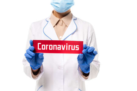 Cropped view of doctor in medical mask holding card with coronavirus lettering isolated on whiteの写真素材