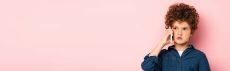 horizontal image of curly boy in denim shirt talking on mobile phone and looking away on pinkの写真素材