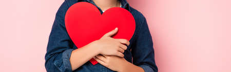 panoramic crop of boy holding heart shape paper cut on pinkの写真素材