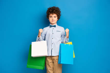curly boy holding shopping bags and standing on blue