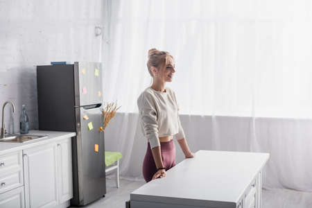 young blonde woman smiling while standing near kitchen table