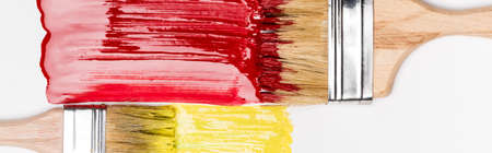 top view of paintbrushes near colorful red and yellow paint brushstrokes on white background, panoramic shotの写真素材