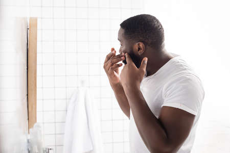 afro-american man trying squeeze pimple in bathroom