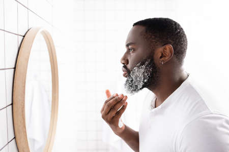 side view of afro-american man applying shaving foam and looking in mirrorの写真素材