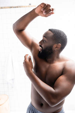 smiling afro-american man with hand up using deodorantの写真素材