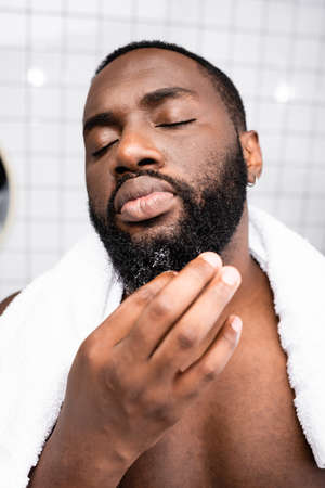portrait of afro-american man using cure for strengthening beard growthの写真素材