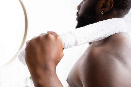 partial view of serious afro-american man looking in mirror with towel behind neck