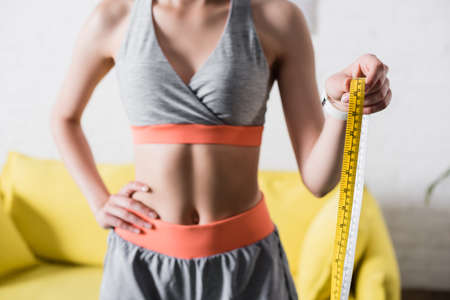 Cropped view of sportswoman with hand on hip holding measuring tape at homeの写真素材