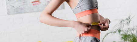 Panoramic orientation of sportswoman measuring waist with tape at homeの写真素材