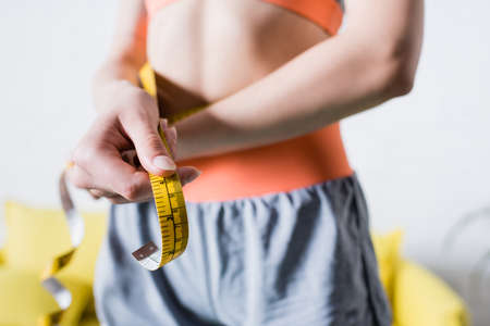 Selective focus of sportswoman with measuring tape at homeの写真素材