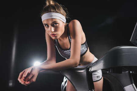 Young sportswoman in headband looking at camera on treadmill in sports center