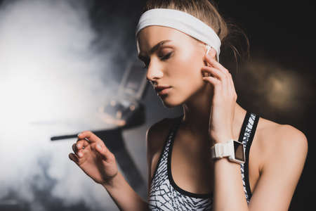 Selective focus of sportswoman with smartwatch touching wireless earphone in gymの写真素材