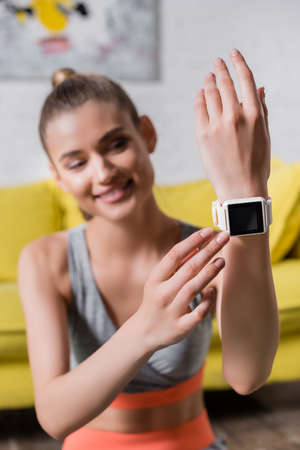 Selective focus of smiling sportswoman touching smartwatch at home