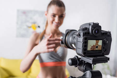 Selective focus of smiling sportswoman pointing at smartwatch near digital cameraの写真素材