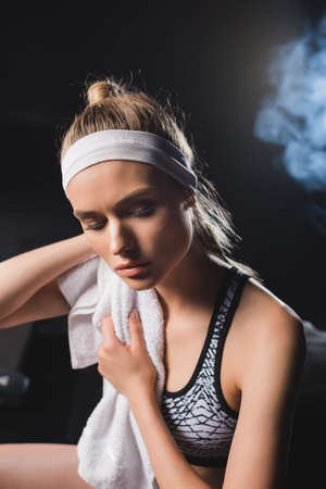 Selective focus of young sportswoman holding towel in gym with smokeの写真素材
