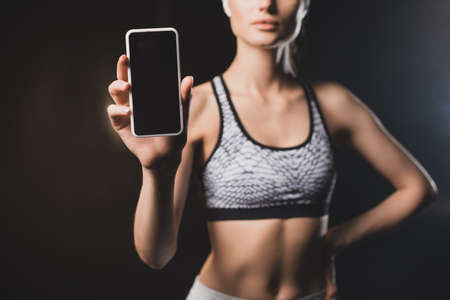 Cropped view of woman showing cellphone with blank screen on black background