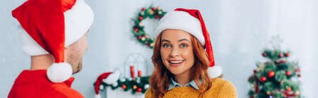 panoramic shot of happy woman in santa hat looking at camera near husbandの写真素材