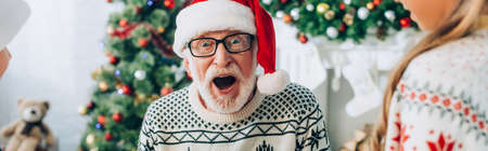 panoramic concept of excited senior man in santa hat near grandchildrenの写真素材