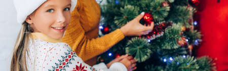 website header of happy girl looking at camera while decorating christmas tree with family