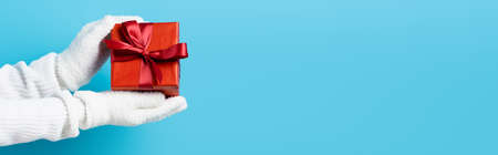 panoramic crop of young woman in gloves holding gift box on blueの写真素材