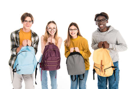 Smiling multicultural teenagers holding backpacks and looking at camera isolated on whiteの写真素材