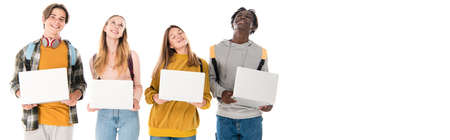 Panoramic crop of positive multicultural teenagers holding laptops isolated on white