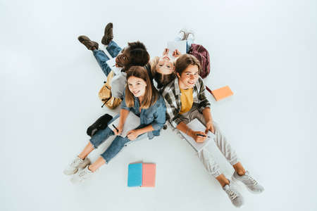 Overhead view of multiethnic teenagers smiling at camera while writing on notebooks on gray backgroundの写真素材