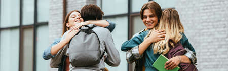 Panoramic orientation of smiling multicultural teenagers with backpacks embracing outdoorsの写真素材