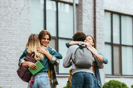 Smiling multicultural teenagers with backpacks embracing outdoors